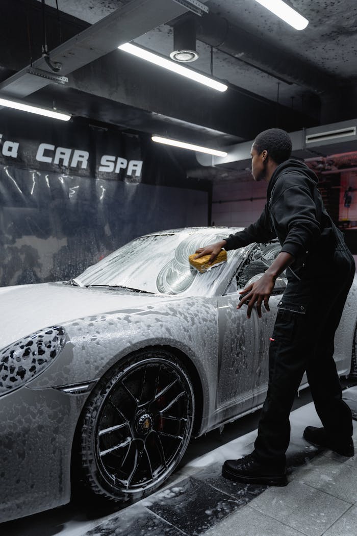 Employee in uniform cleaning a luxury car with foam at an indoor car spa.